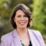 Rebecca Barry smiling in a lavender blazer with a blurred green outdoor background