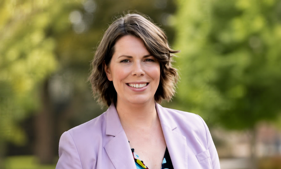 Rebecca Barry smiling in a lavender blazer with a blurred green outdoor background